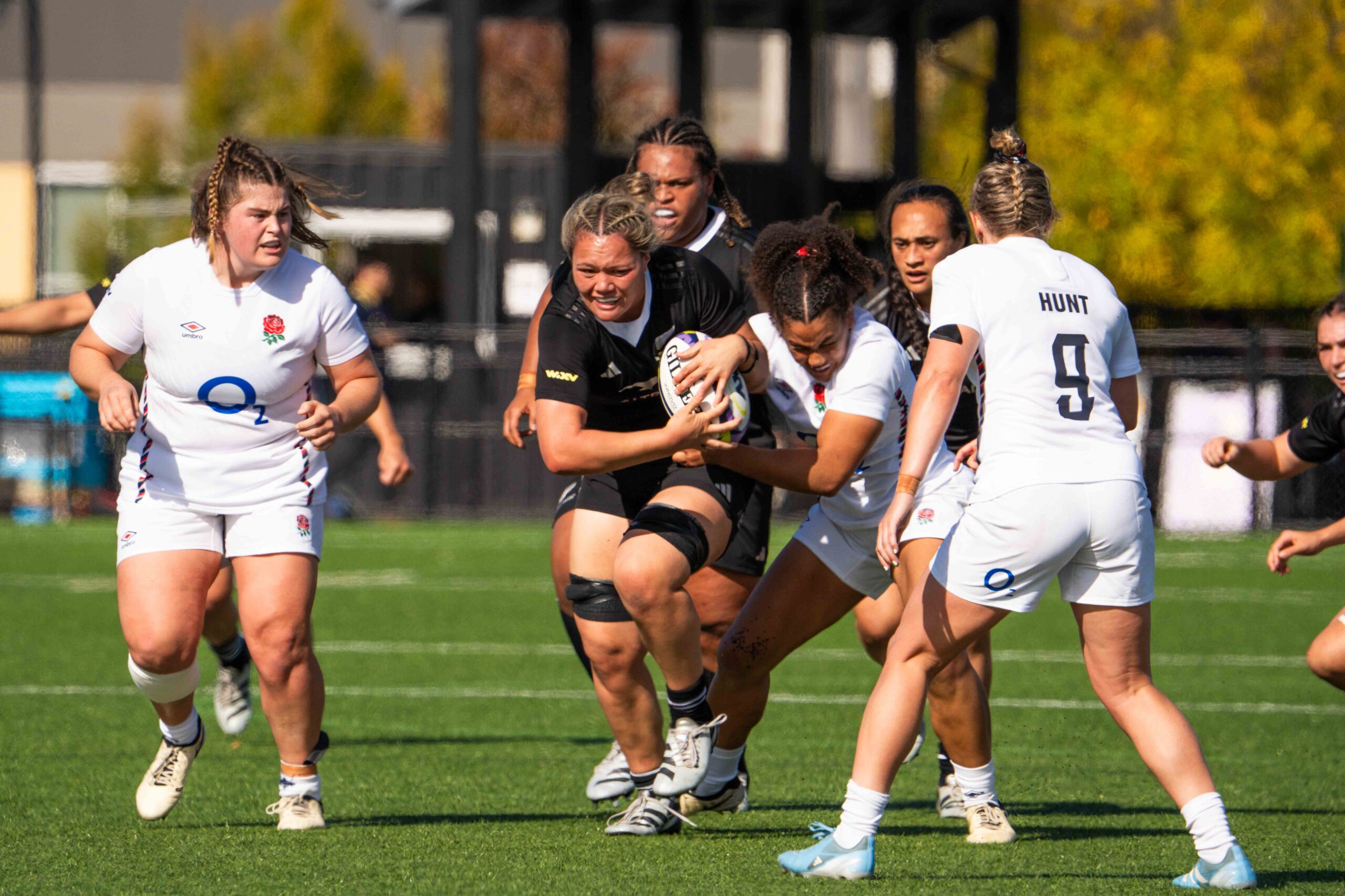 New Zealand Black Ferns player carrying the ball while being tackled by England players.