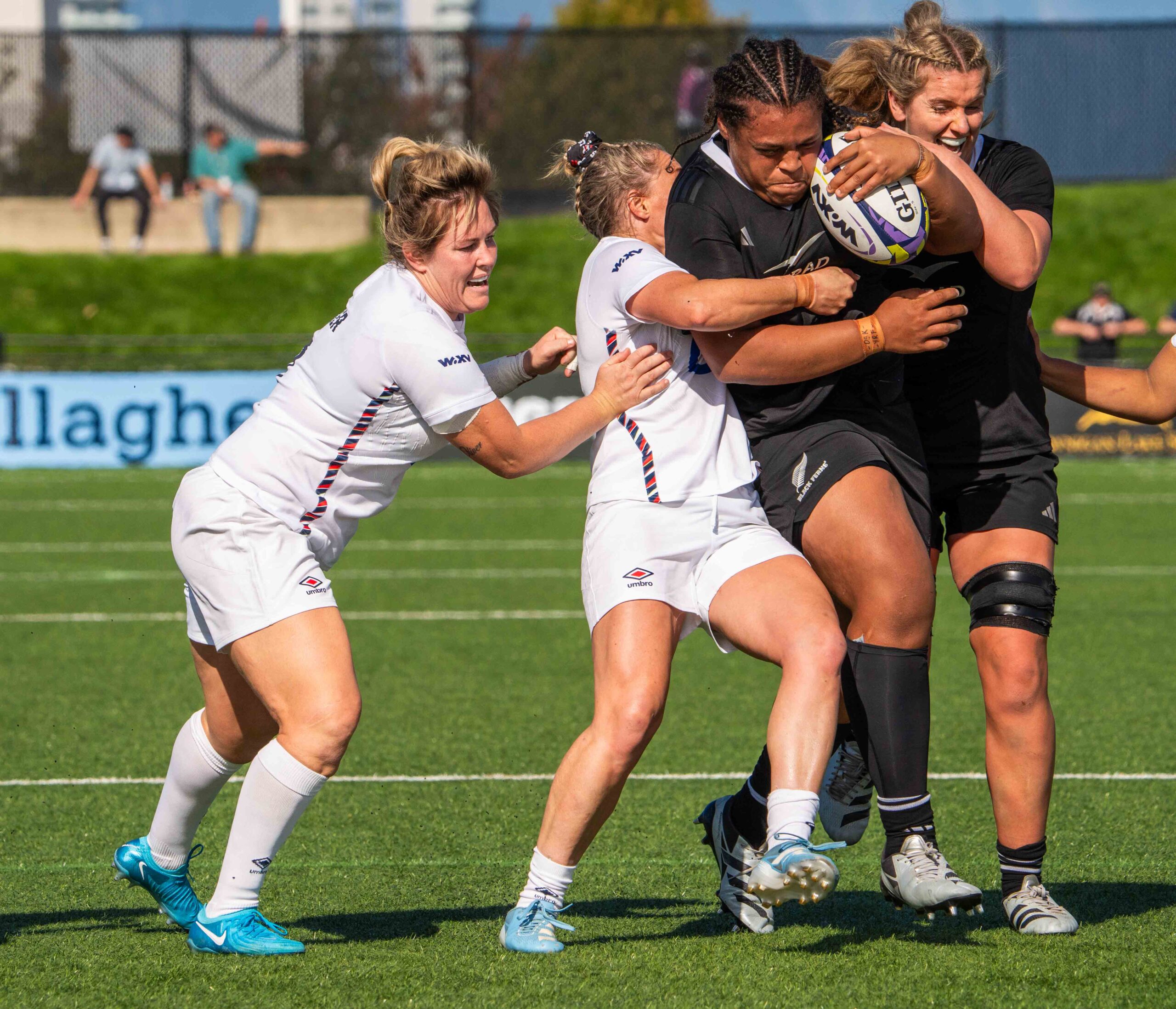Action shot of a rugby ball in the air with players from England and New Zealand tracking its flight.