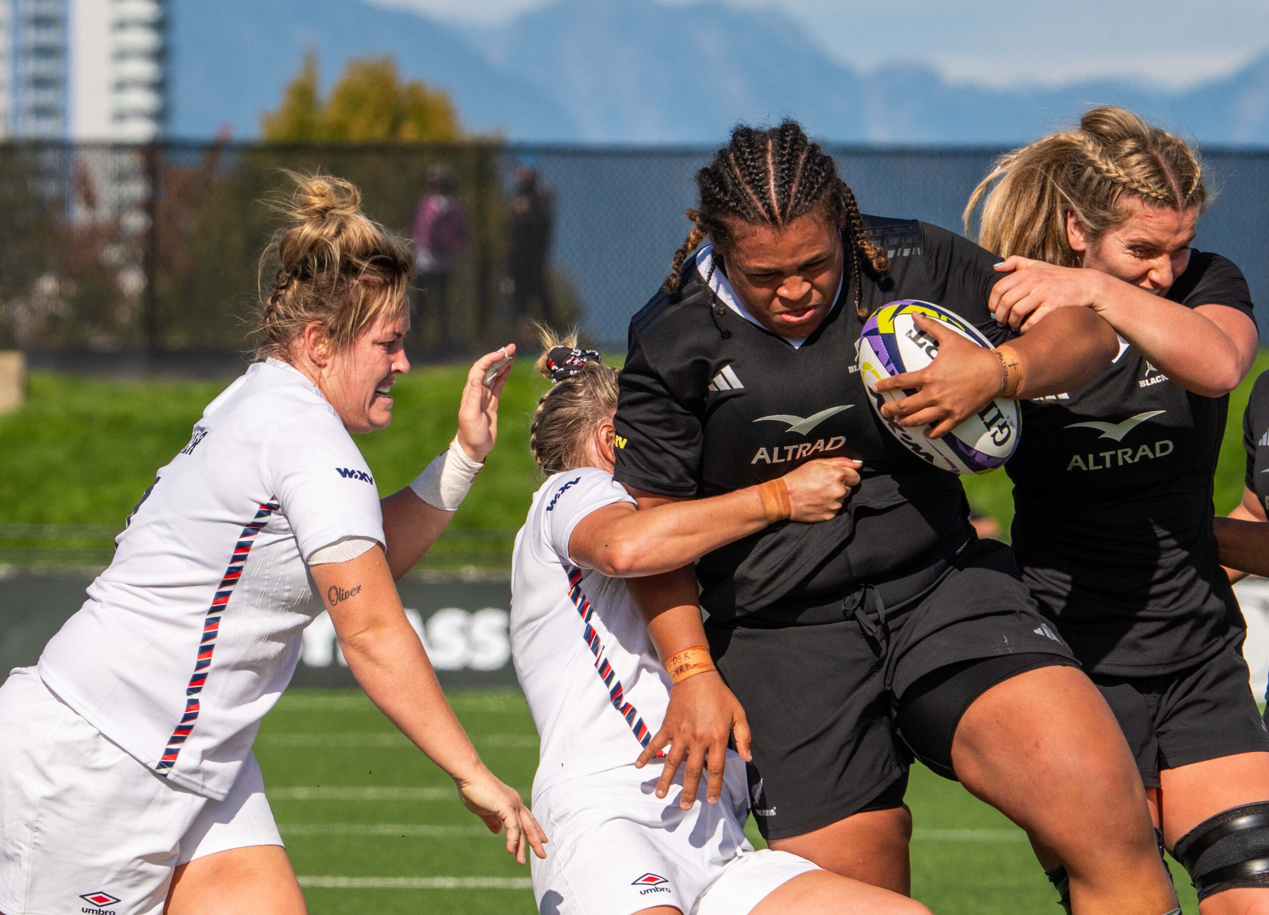 England and New Zealand rugby players sprinting toward a loose ball on the grass pitch.