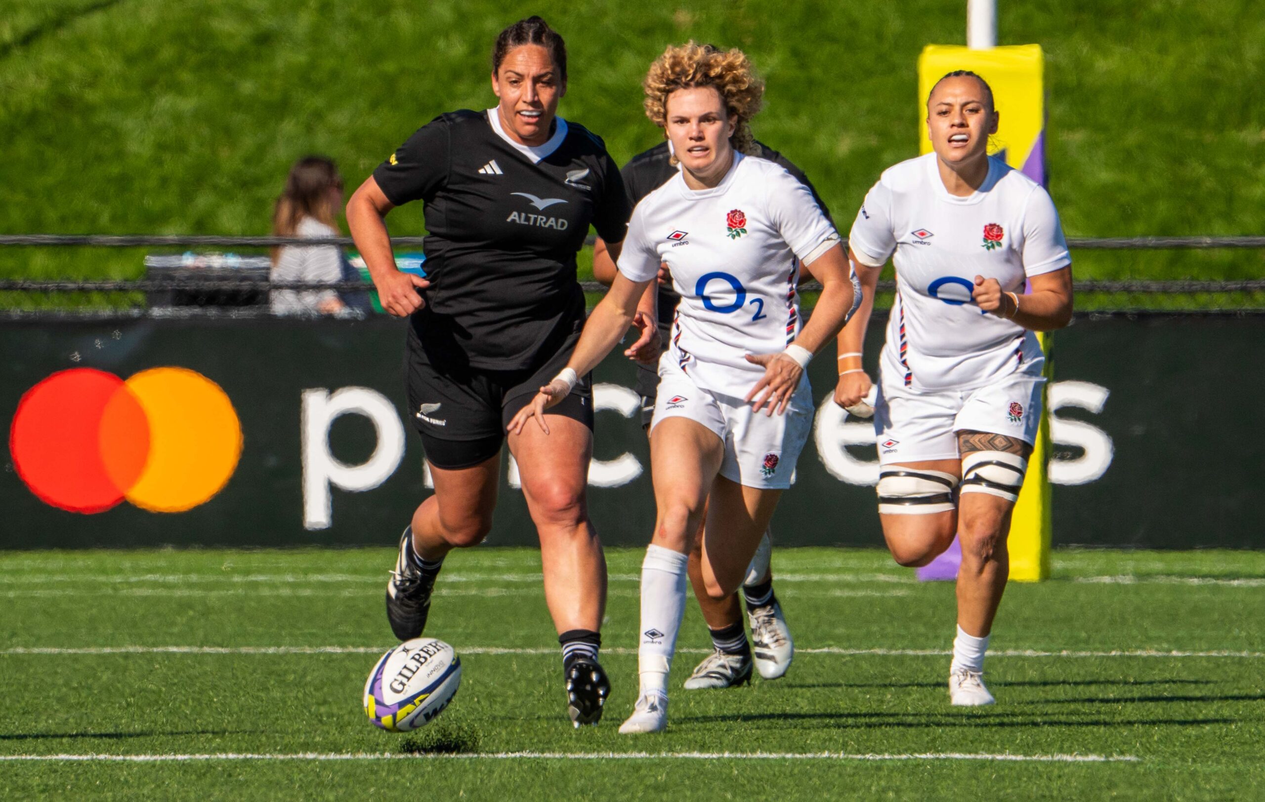 Close-up action shot of a New Zealand rugby player breaking through a tackle by English defenders.