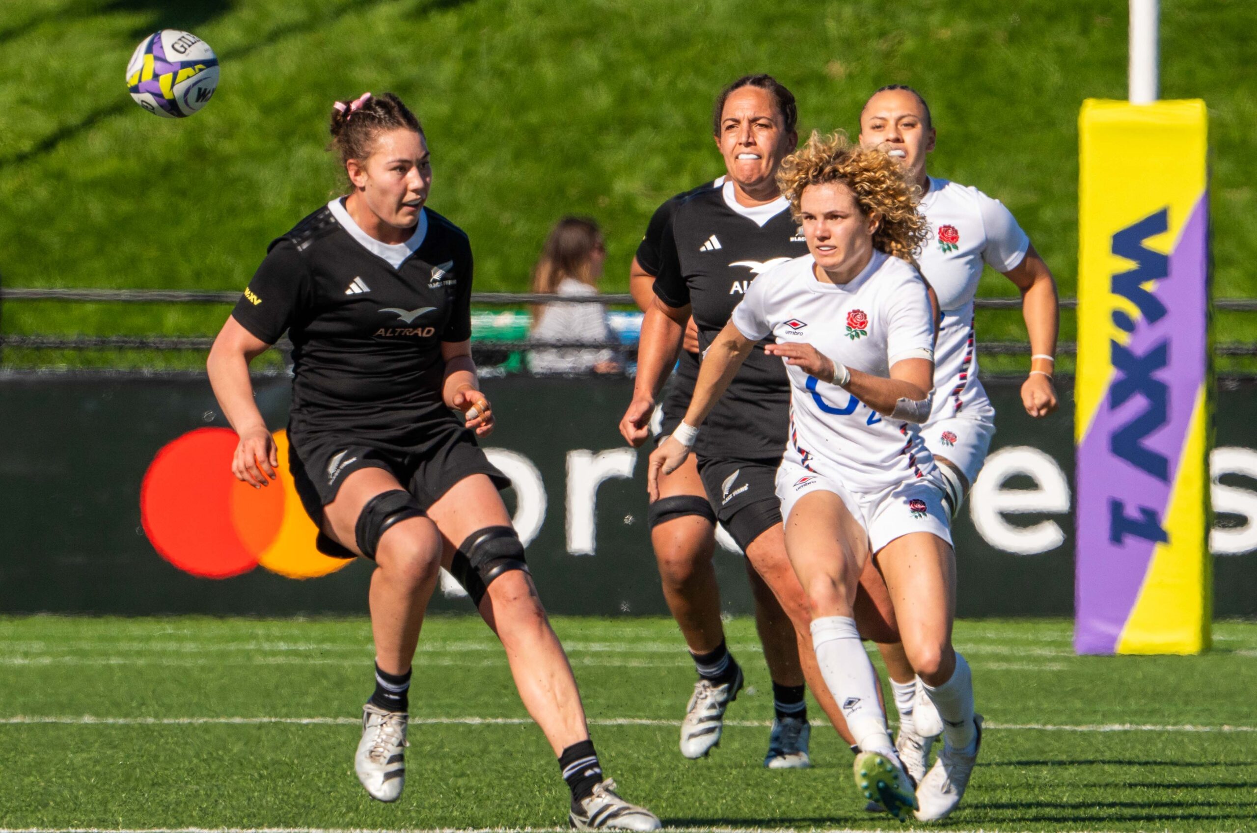 Three rugby players in a high-intensity tackle during a New Zealand Black Ferns vs England match.