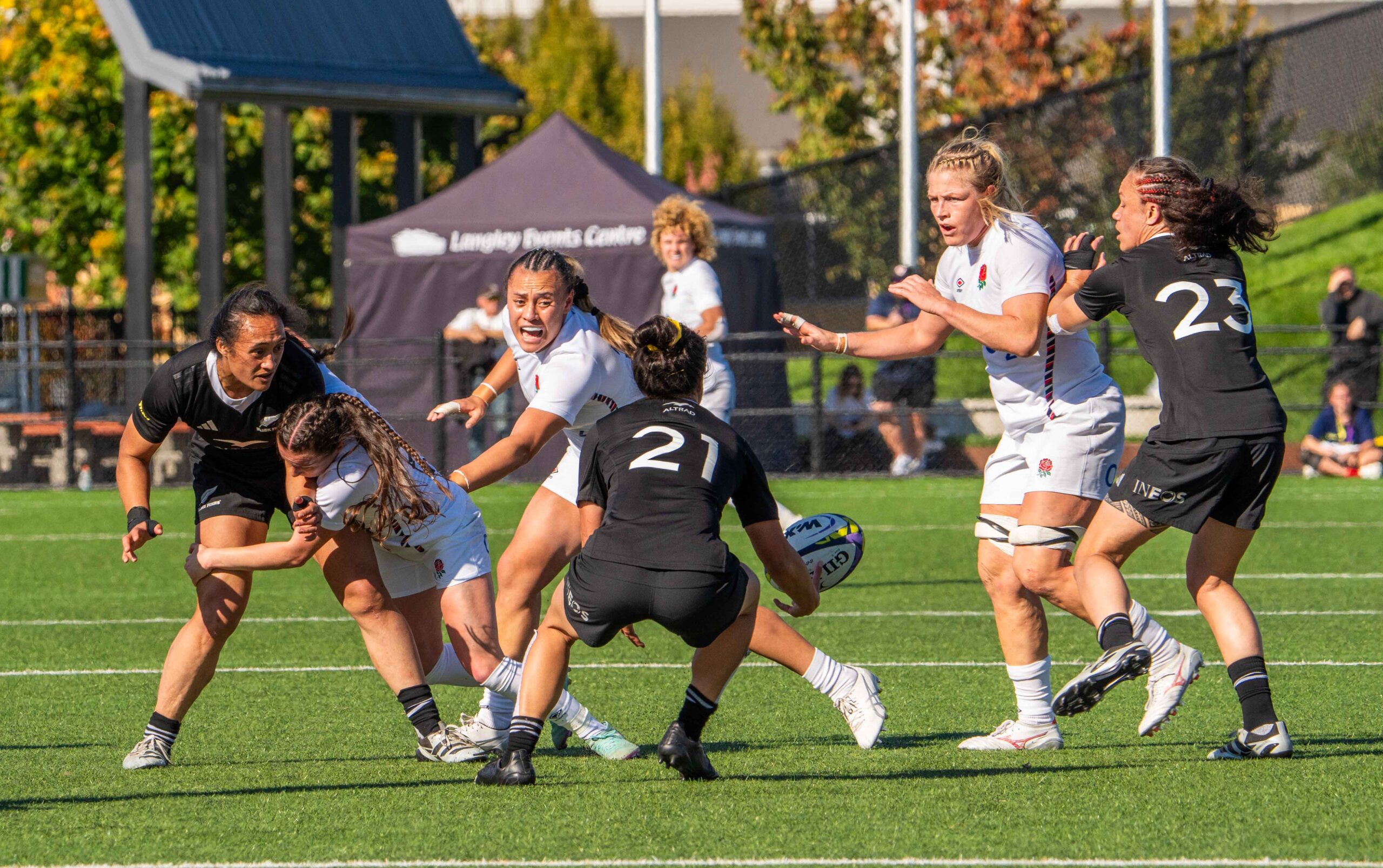 Action shot of a New Zealand rugby player being tackled by England defenders during a match.