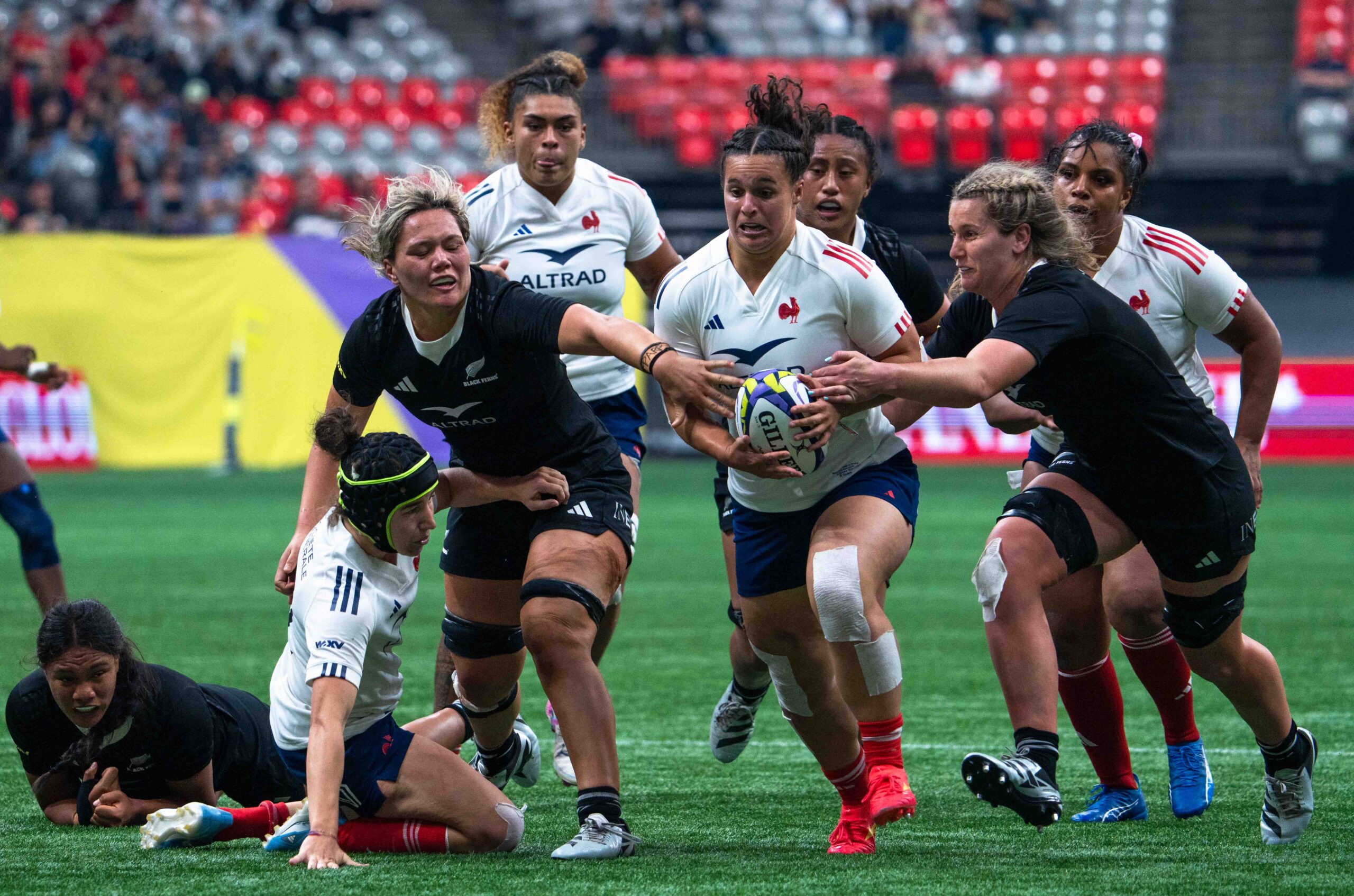 Intense match action between France and New Zealand Women's Rugby Union teams in a stadium.