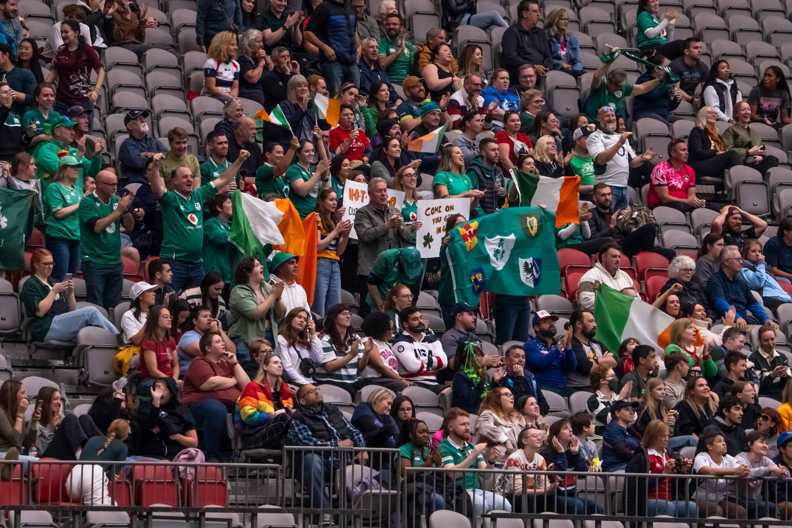 Crowds of fans in a stadium waving Irish flags and holding "Come on you Girls in Green" signs.