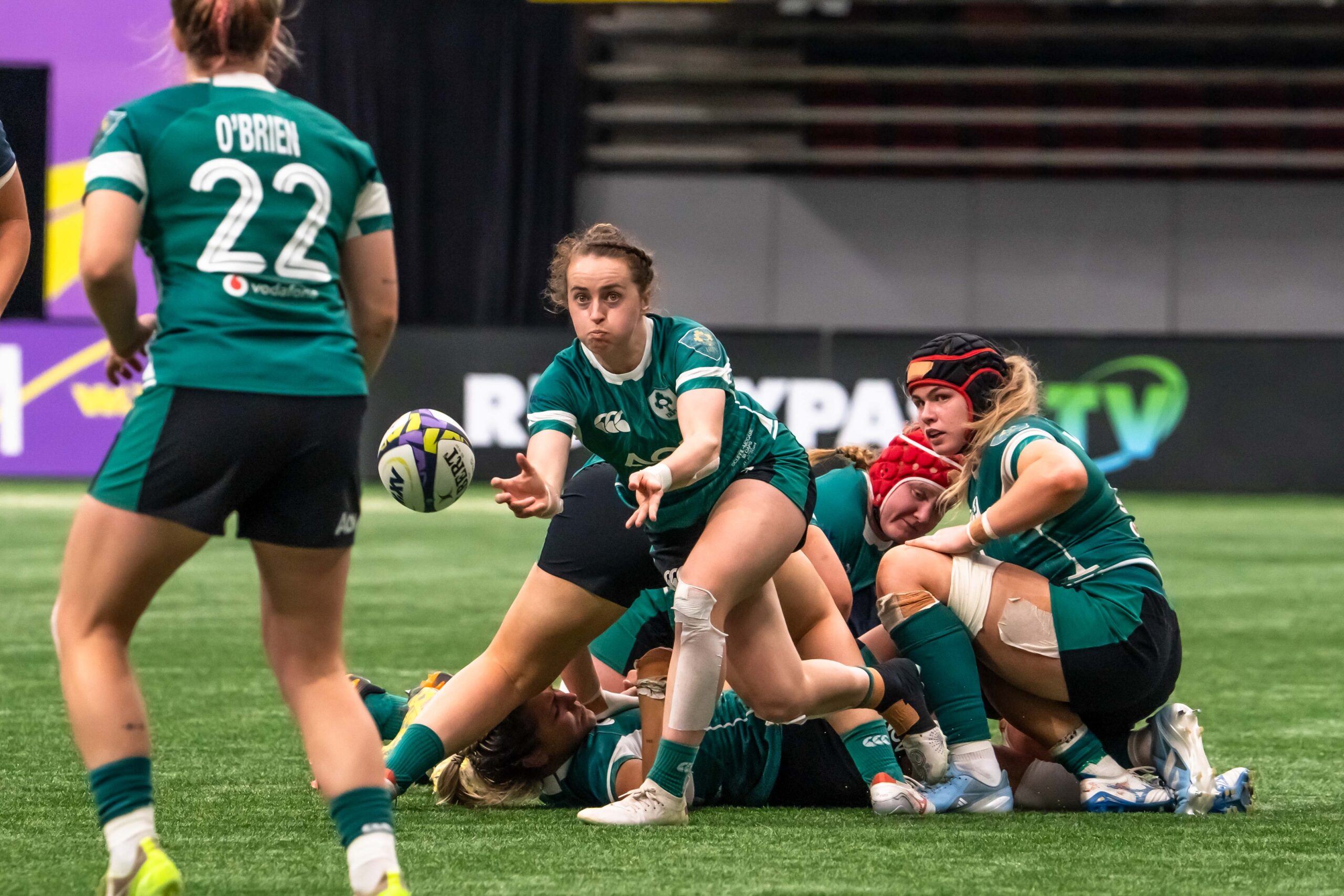 An Irish rugby player in a green AON jersey passing the ball from the base of a ruck.