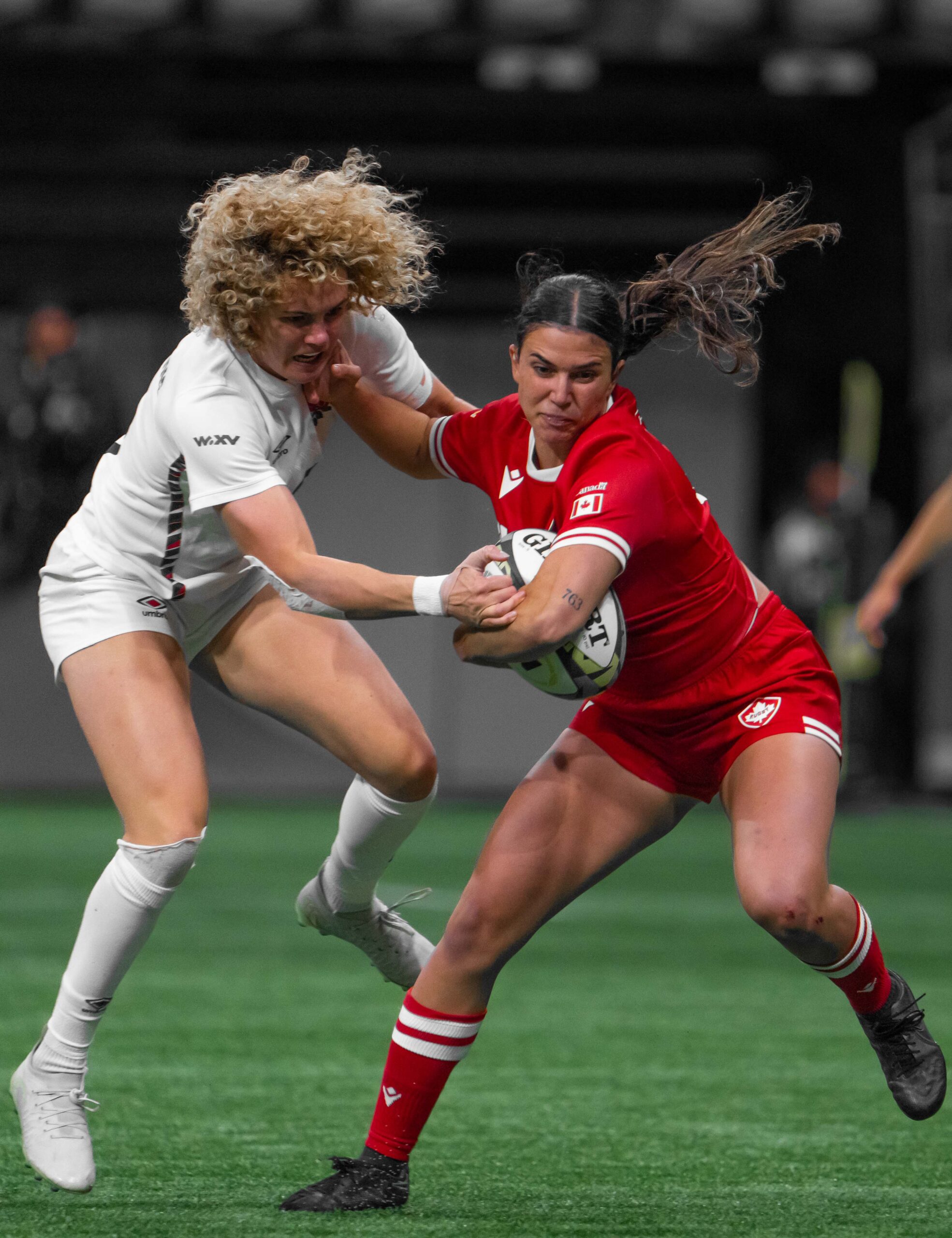 Canada women's rugby player executing a strong fend against an England defender in open play.