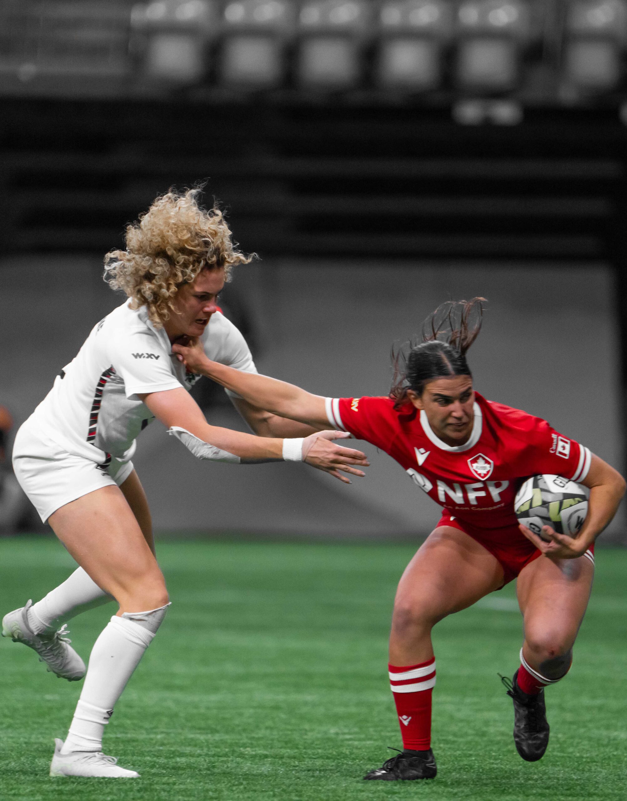 Canada ball carrier driving through England's defensive line during a WXV 1 rugby match.
