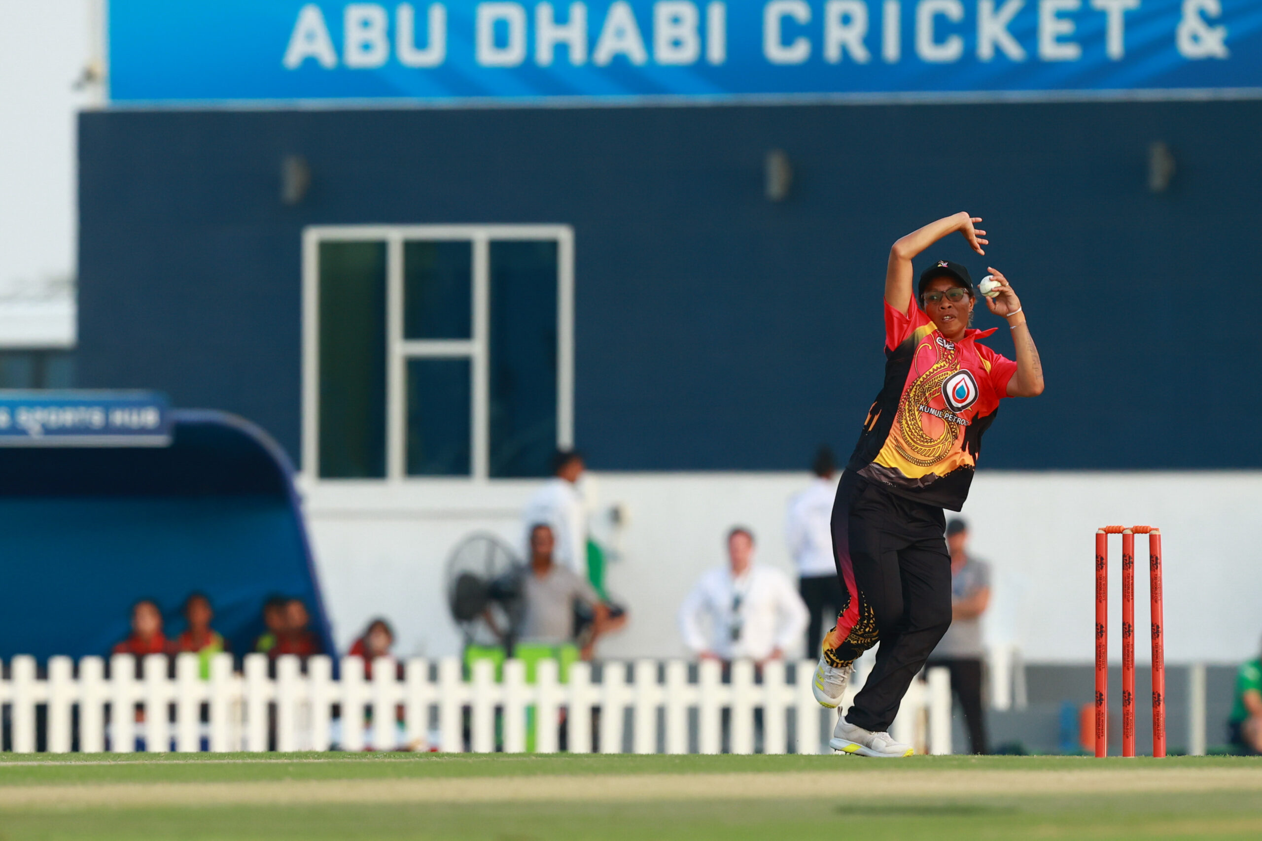 International women's cricket bowler in mid-action at the Abu Dhabi Cricket & Sports Hub stadium.