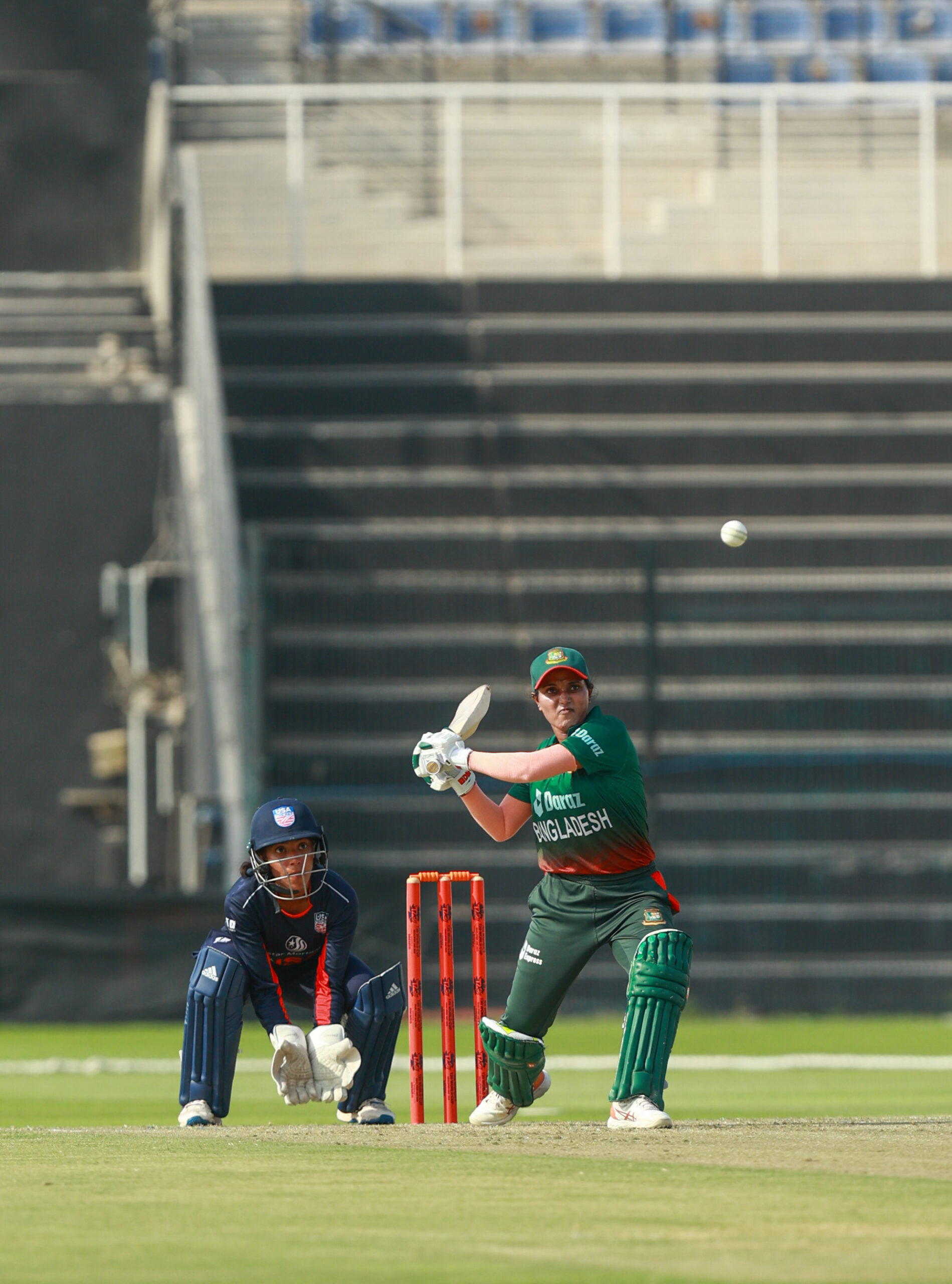 Bangladesh women's cricket team batter playing a shot against USA at a Dubai sports stadium.