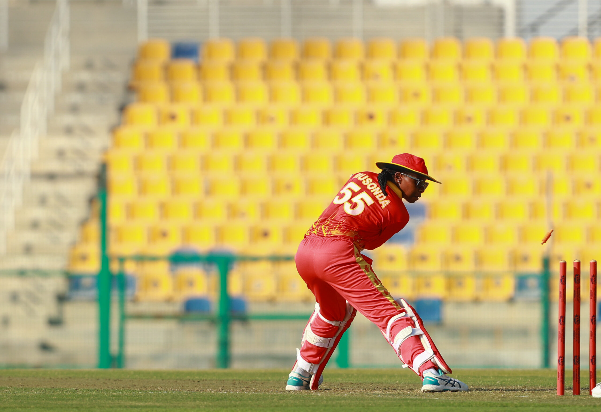 Zimbabwe women’s national cricket team batter playing a sweep shot during an international match at a Dubai cricket stadium, featuring a wicketkeeper and yellow stadium seating