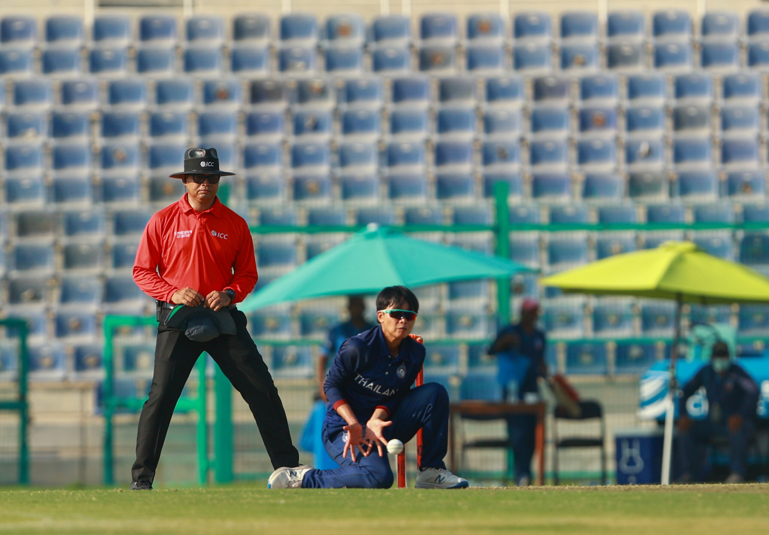 Thailand women's wicketkeeper in a crouching position waiting for the ball with an ICC umpire standing behind.