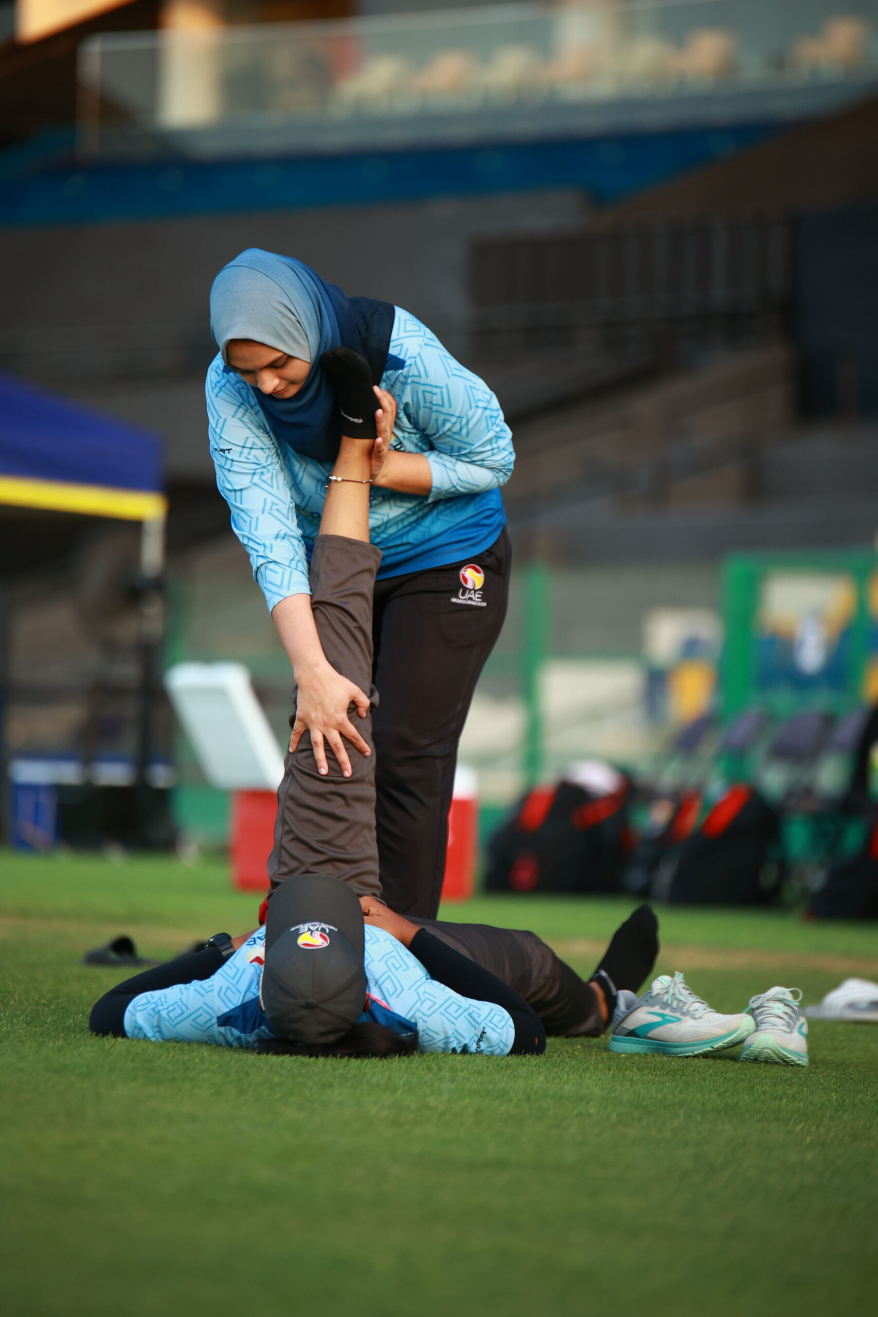 UAE women’s cricket player receiving a hamstring stretch from a trainer on the field before a match.