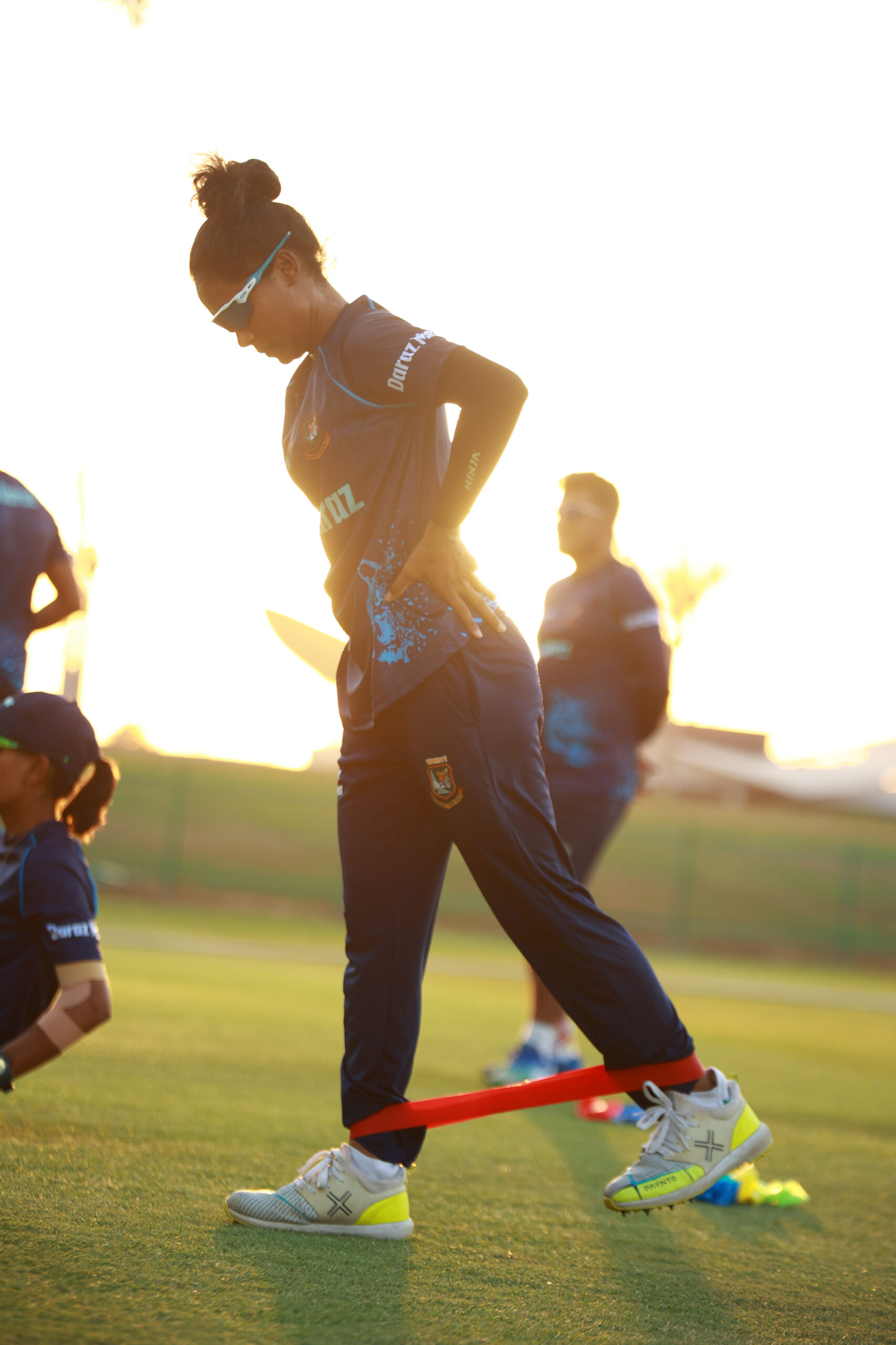 A Bangladesh female cricketer using a red resistance band for glute and hip activation during training in Dubai.