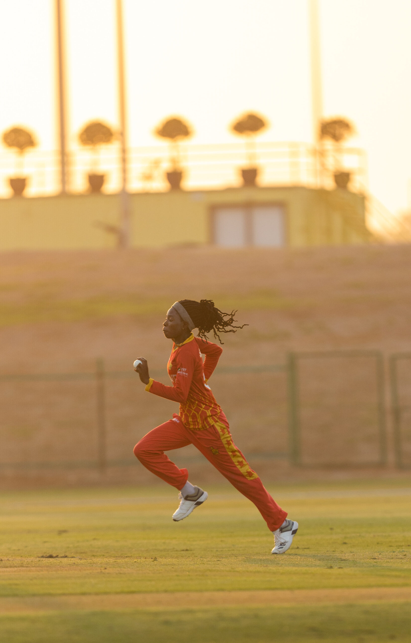 Professional female cricket bowler running in to bowl during a match at sunset in Dubai.