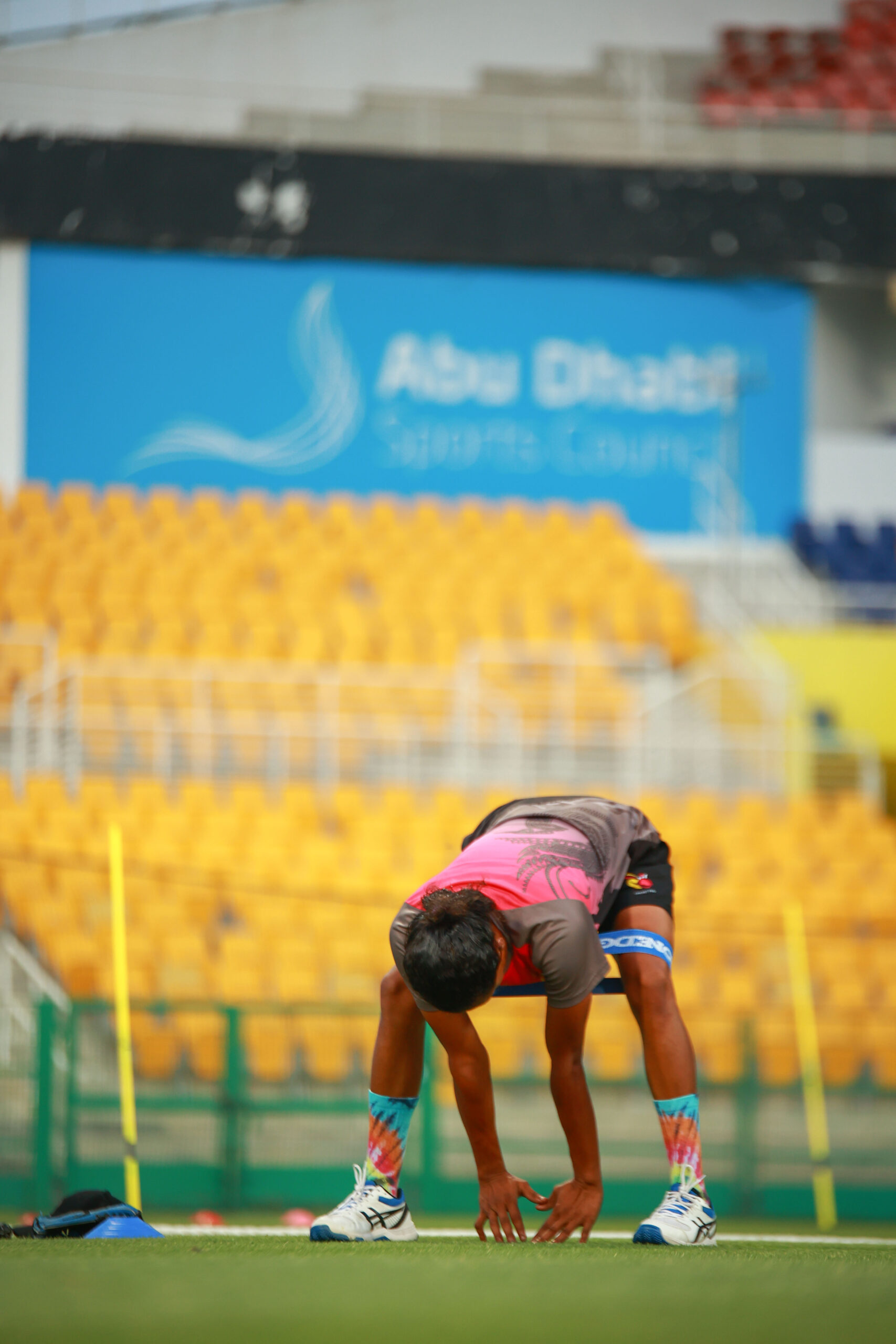 Female cricketer performing a resistance band warm-up stretch at Zayed Cricket Stadium, Abu Dhabi.