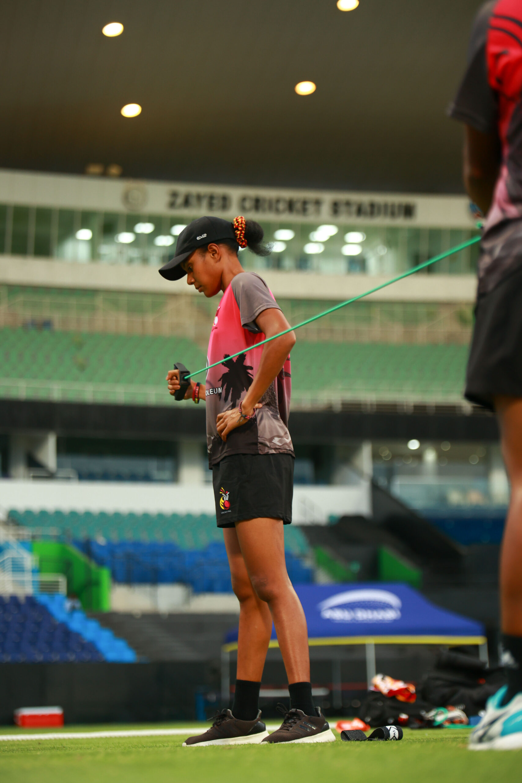 Professional cricketer using a green resistance band for upper body strength training at Zayed Cricket Stadium.