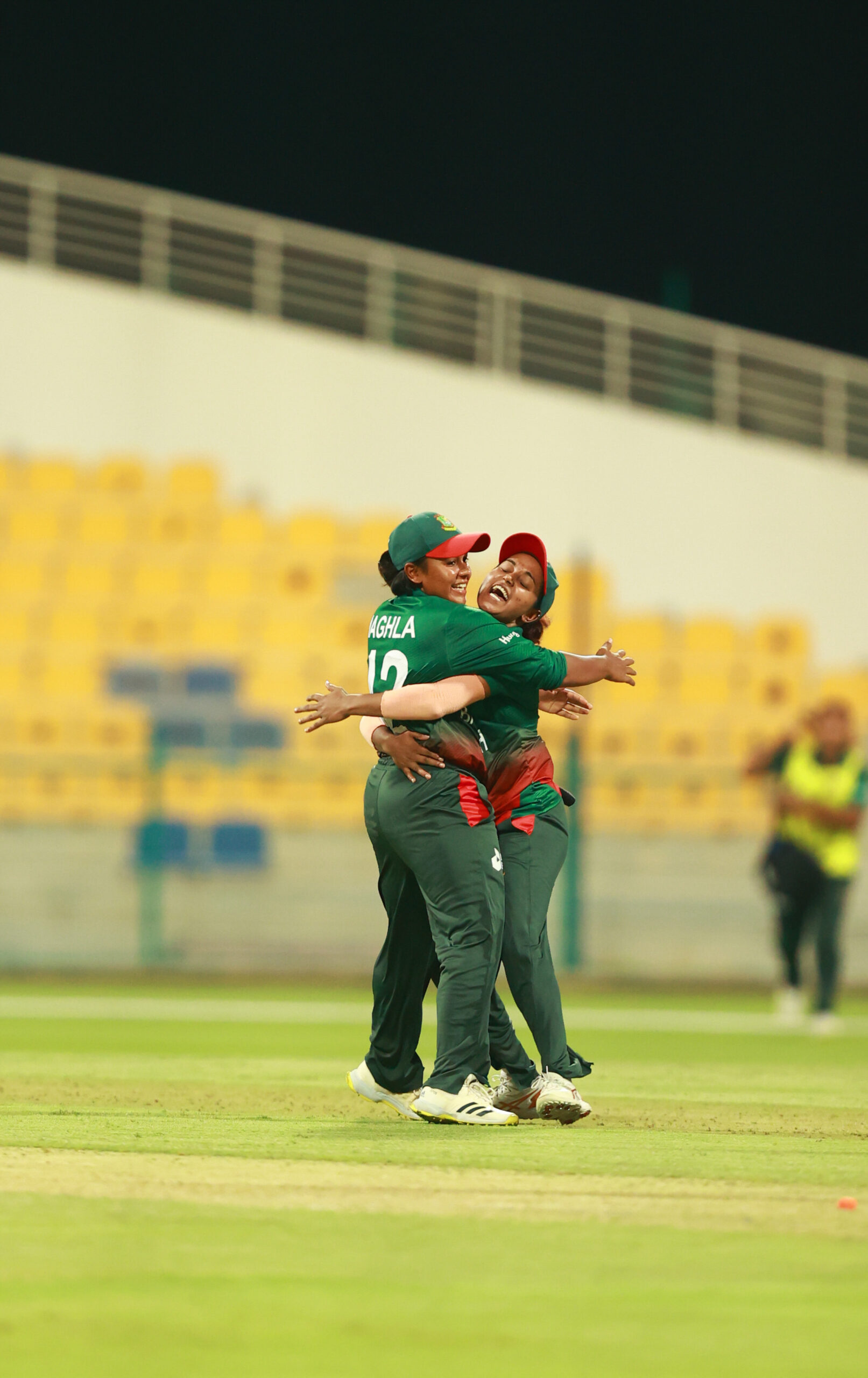 Bangladesh women’s cricketers hugging in celebration after a victory at a cricket stadium.