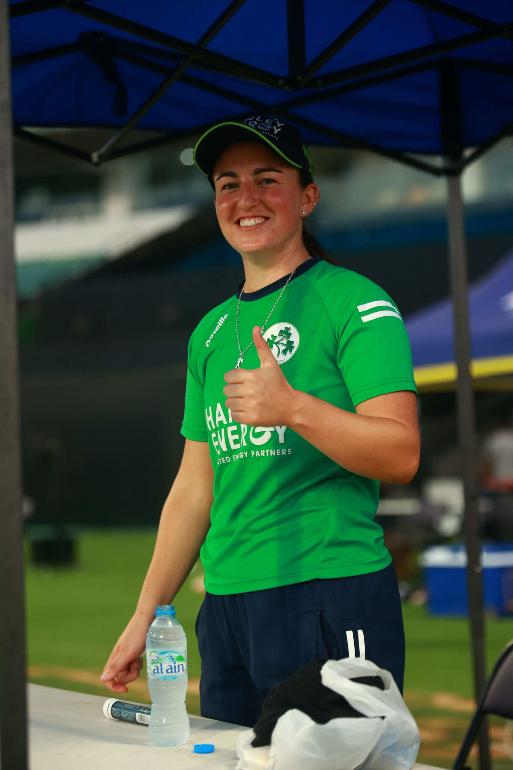 Ireland women’s cricket player in a green Hanley Energy jersey giving a thumbs up at a Dubai stadium.