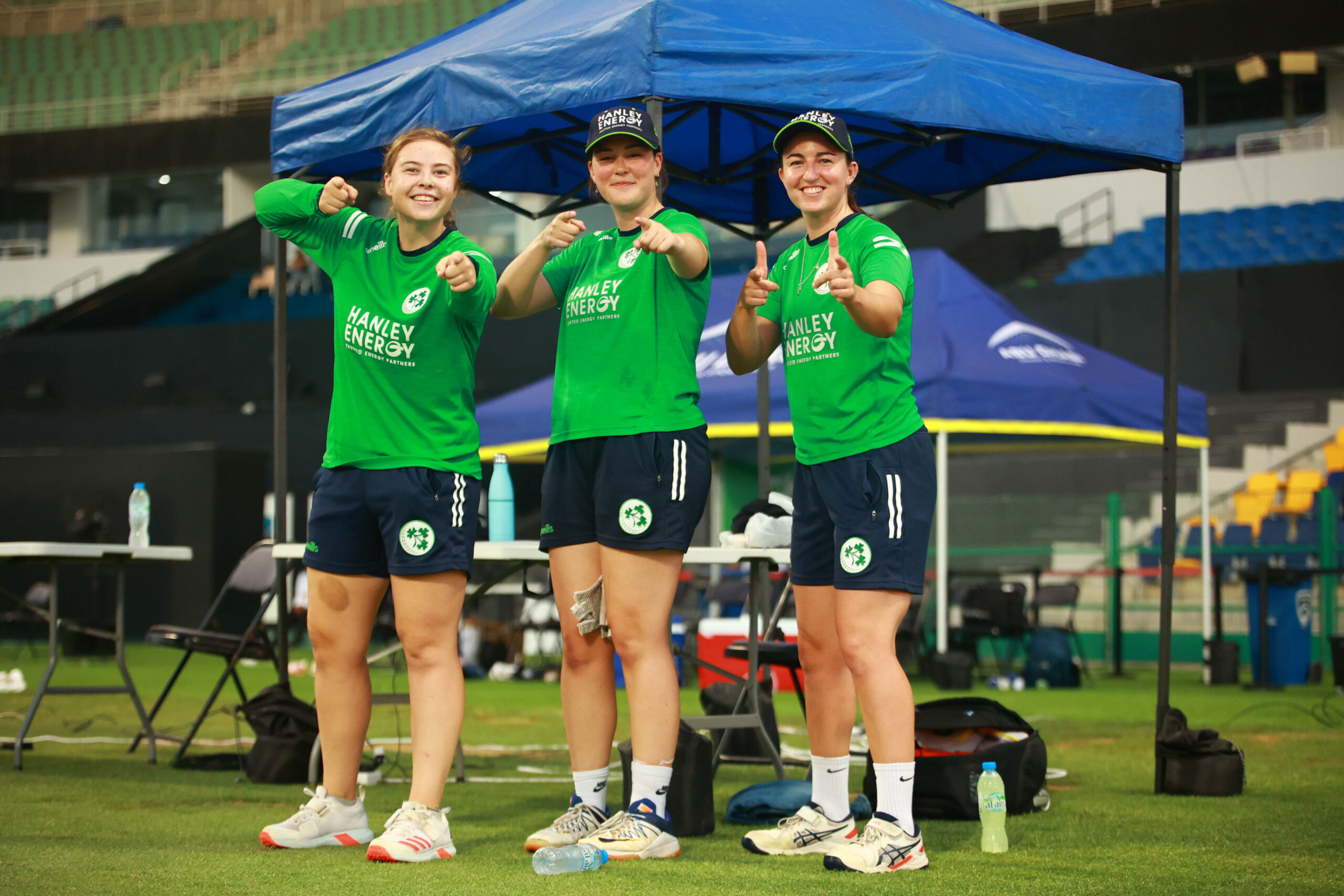 Full-length shot of three Ireland cricketers in green jerseys and navy shorts posing at a stadium in Dubai.