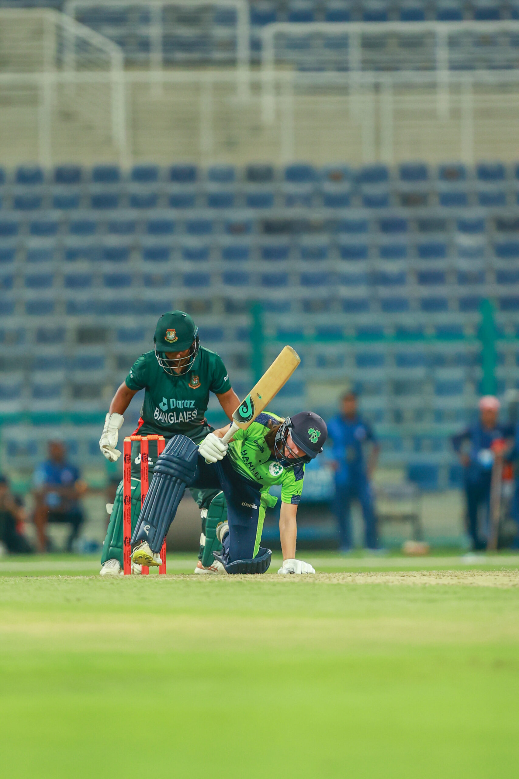 Bangladesh wicketkeeper watching an Ireland batter miss a shot during a night cricket match in a stadium.